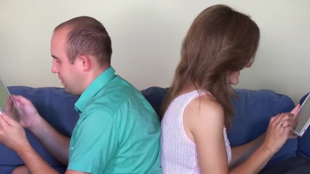 Marido e esposa usando próprios computadores tablet sentado no sofá de costas para trás — Vídeo de Stock