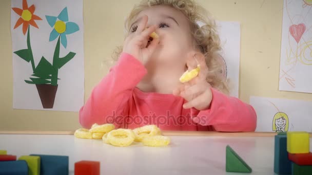 Hongerig kind eten maïs maïs chips zitten in de buurt van tabel in zijn kamer — Stockvideo