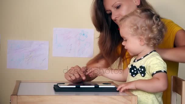 Мама помочь своей девочке с помощью планшетного компьютера, сидя за столом . — стоковое видео
