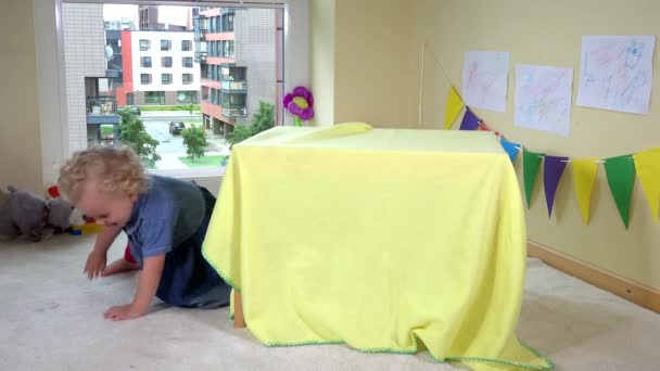 Nettes Mädchen versteckt sich zu Hause unter einem Tisch, der mit Wrap bedeckt ist — Stockvideo