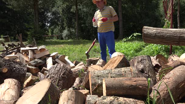 Tired farmer man drink water from plastic bottle and chop wood. 4K — Stock Video