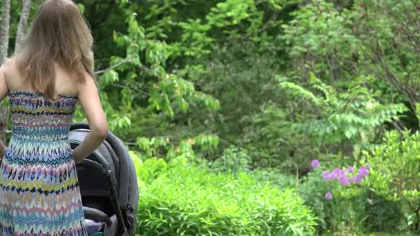 Elbiseli kadın bebek çocuk arabası bahçesinde uyku için göndermek deneyin. 4k — Stok video