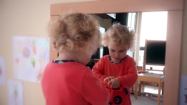 Adorable niña poner gafas de sol rojas en la cabeza cerca del espejo — Vídeos de Stock