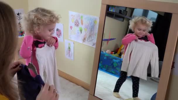 Маленькая девочка измеряет одежду перед зеркалом — стоковое видео