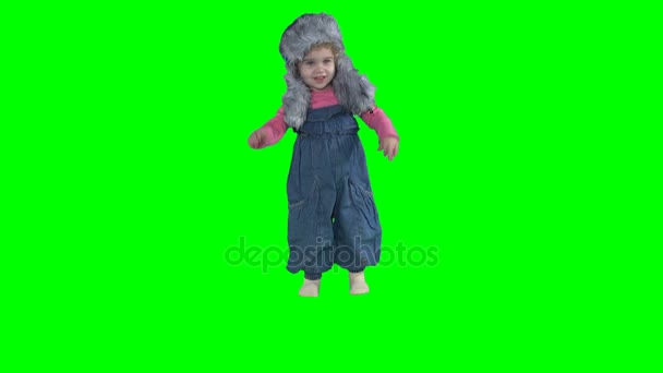 Чарівна дівчинка-малюк стрибає з теплим зимовим капелюхом ізольовано на зеленому — стокове відео