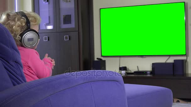 Bella ragazza che ascolta musica con le cuffie e guarda la TV. Schermo verde . — Video Stock