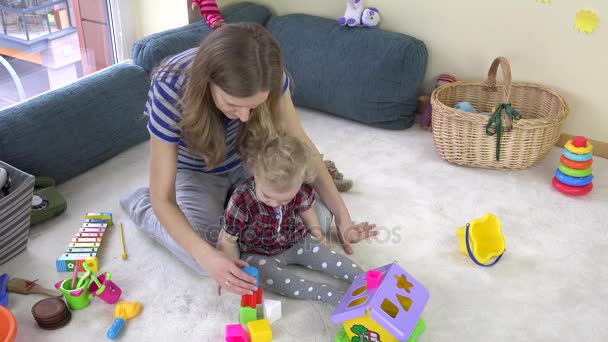 Vrouw met peuter meisje proberen te maken van speelgoed bakstenen toren. — Stockvideo