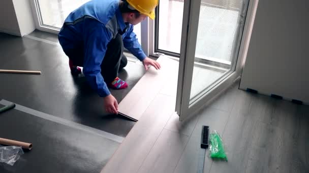 Geschickter Handwerker mit gelbem Hut installiert Laminatplatten auf dem Fußboden — Stockvideo