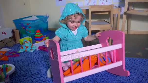 Menina hiperativa balançar sua boneca bebê aproximadamente na cama de brinquedo — Vídeo de Stock