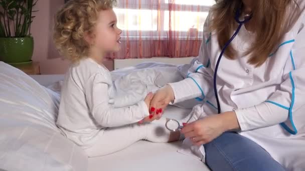Mulher médico enfermeira examina doente pequena menina adorável com estetoscópio na cama — Vídeo de Stock