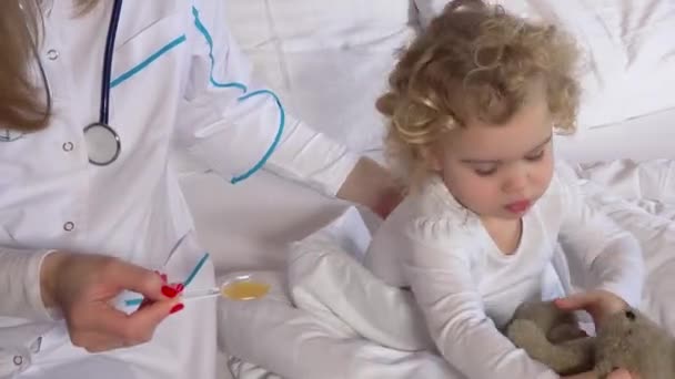 Doctor woman giving child patient remedy with spoon sitting with teddy bear — Stock Video