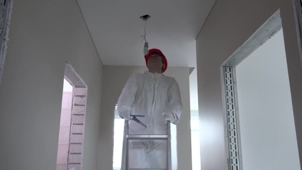 Електрик з шоломом піднімається по сходах і відкручує лампочку — стокове відео