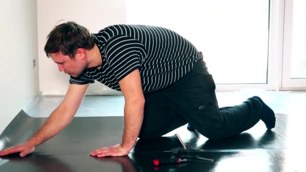 Homem trabalhador masculino cuidadoso que estabelece underlay para a instalação de piso laminado — Vídeo de Stock