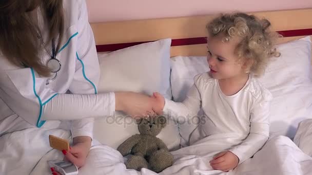 Femme médecin et petite fille enfant patient poignée de main et mesurer la température — Video