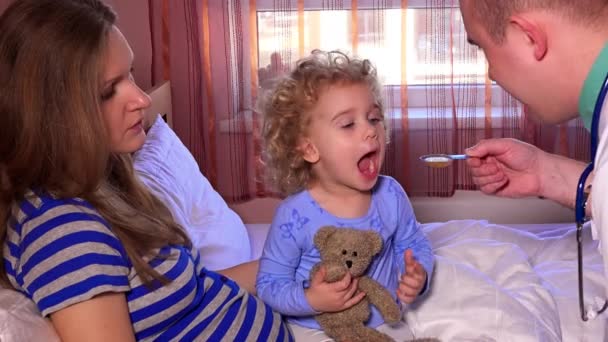 Orvos ember gyógyszer kanál adva a gyermek ült az ágyban az ő édesanyja — Stock videók
