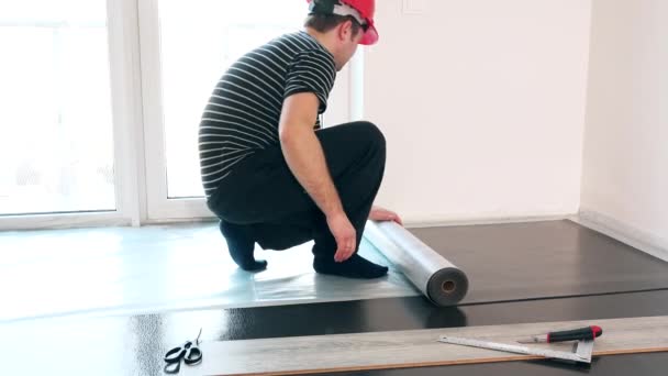 Skilled guy with red helmet lay sub-flooring mat in new apartment — Stock Video