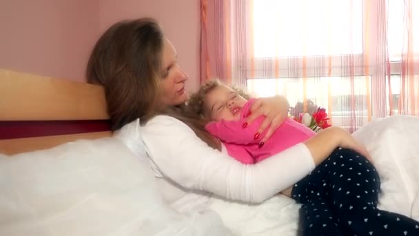 Joven madre sosteniendo y balanceando a su niña en la cama — Vídeos de Stock