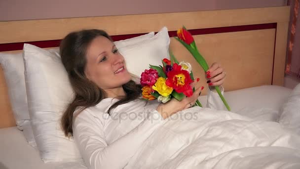 Menina mulher atraente deitado na cama com flores de tulipa e olhando para a câmera — Vídeo de Stock