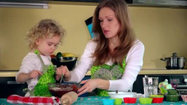 Anne gülümseyerek ve ders kızı mutfakta ev yapımı kek hamuru hazırlamak