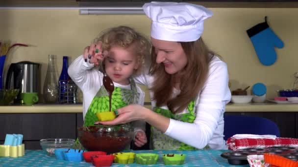 Schöne Tochter hilft ihrer Mutter, Muffinformen mit Teig zu füllen — Stockvideo