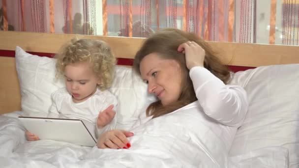 母亲和蹒跚学步的女儿躺在床上与平板电脑 — 图库视频影像