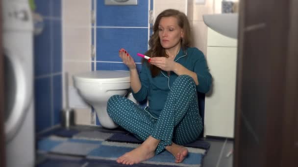 Woman sitting on floor in bathroom holding pregnancy test with two stripes — Stock Video