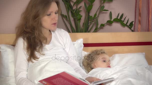 Aranyos kis lány feküdt az ágyban, miközben a nő anya olvassa el a könyv mese — Stock videók