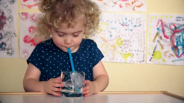 Grappig meisje spelen met stro en glas water zitten door tabel in haar kamer — Stockvideo