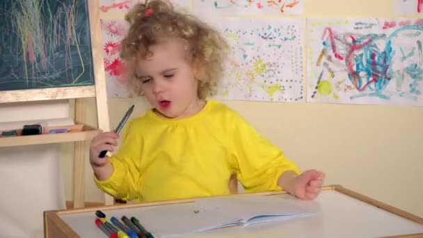 Emocional niña rubia dibujar con lápiz en el libro sobre la mesa — Vídeos de Stock