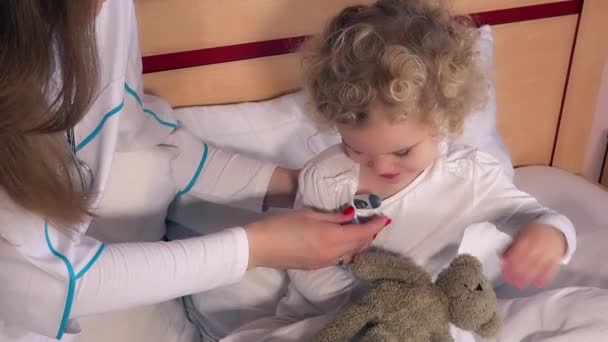 Любопытный ребенок с женщиной врач смотрит на термометр после измерения температуры — стоковое видео
