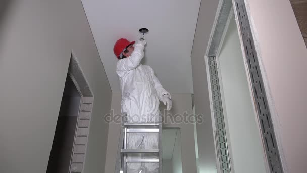 Ouvrier debout sur l'échelle et le trou de coupe dans le plafond du couloir — Video