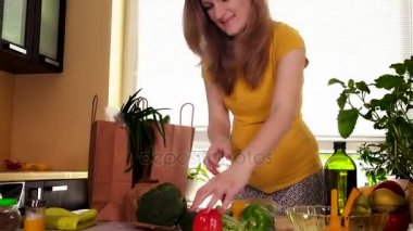 Genç hamile eşi kaldırma alışveriş çantası mutfak masasında doğal sebze