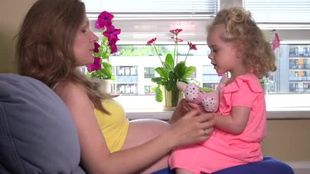 Těhotná žena a dcera roztomilé blond dívka hrát s hračkou panenka doma — Stock video