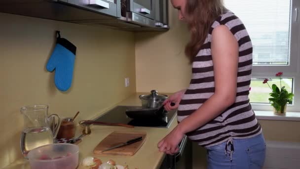 Gravid kvinna laga mat i köket matlagning pan på kokplatta — Stockvideo