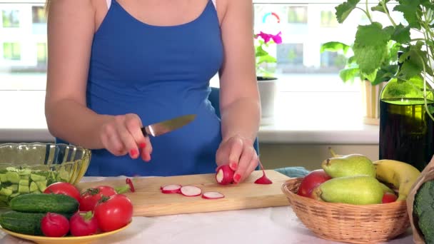 Беременная женщина режет редьку на доске — стоковое видео