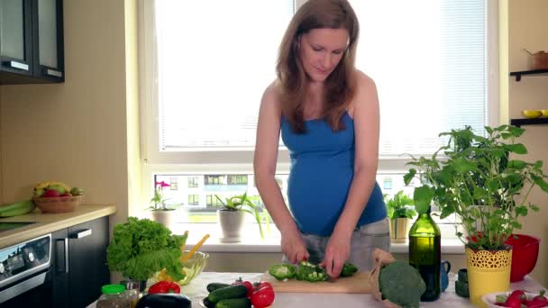 Mladá těhotná žena krájení zelenou paprikou a chuť to při pohledu na fotoaparát — Stock video