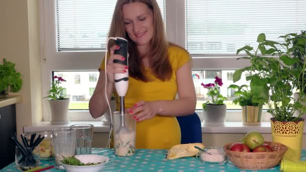 Процесс приготовления зеленого фруктового коктейля. Беременная женщина с блендером — стоковое видео