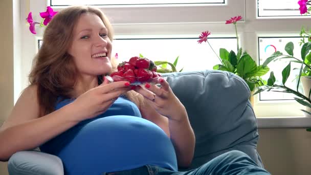 Mujer bastante embarazada comiendo fresas y sonriendo mirando a la cámara — Vídeo de stock