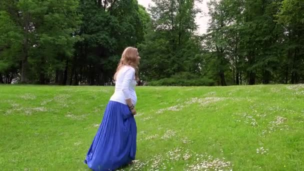 Беременная женщина, гуляющая по лугу парка в солнечный летний день — стоковое видео