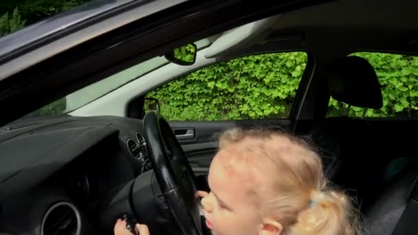 Child pretends driving car sitting on front driver seat with hands on steering — Stock Video