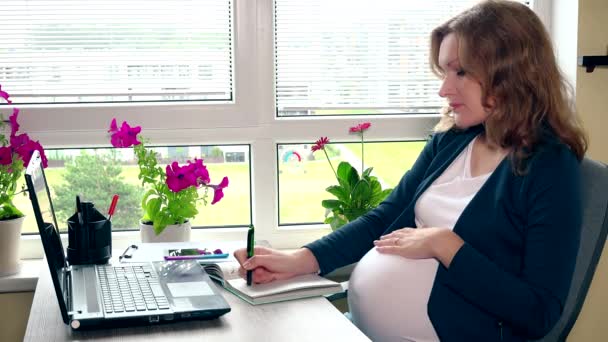Беременная деловая женщина пишет заметки. Беременная зрелая женщина, работающая в офисе — стоковое видео