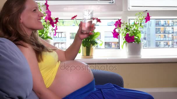 Муж мужчина рука дать стакан воды для его беременной жены женщина сидит на диване — стоковое видео