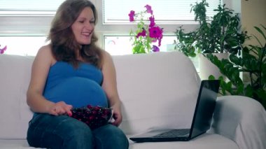 Hamile kadın kiraz çilek yemek ve bilgisayar görüntülü konuşma konuşmak