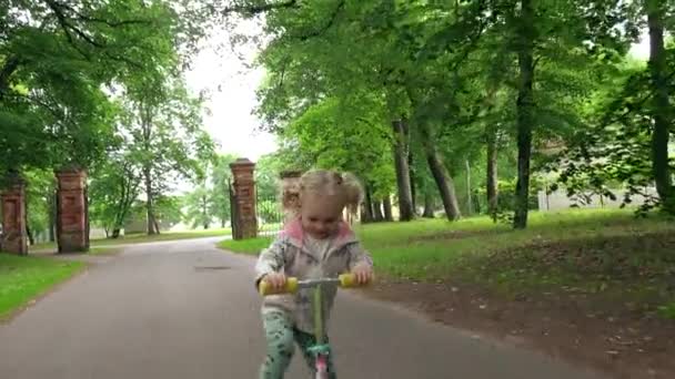 Маленький ребенок катается на скутере в парке в летний день. Милая девушка играет на открытом воздухе — стоковое видео