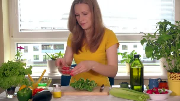 Вагітна жінка їсть маленькі помідори, сидячи біля столу на кухні — стокове відео