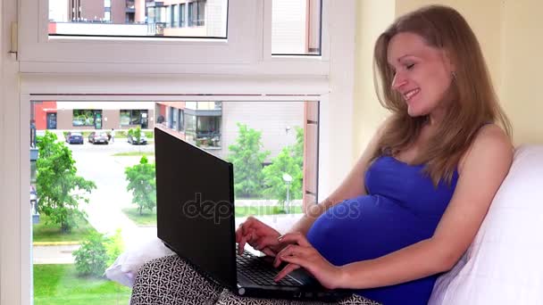 Щаслива вагітна майбутня матуся з портативним комп'ютером. Жінки розважаються вдома — стокове відео