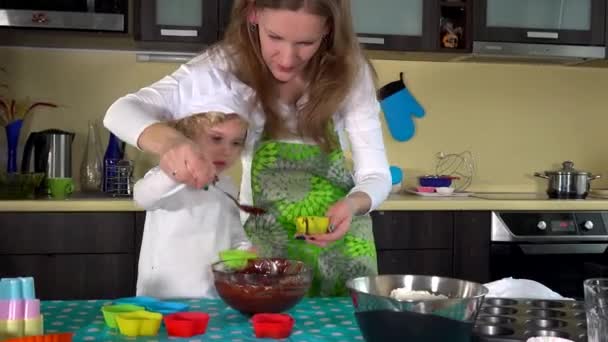 Schattig meisje en mooie moeder zijn spooning muffin beslag in baking cups — Stockvideo