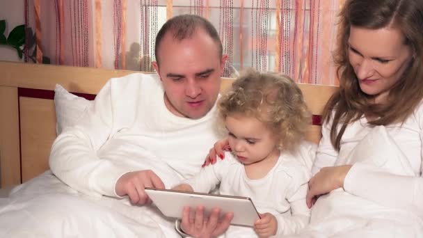 家庭夫妇与他们的小女儿女孩躺在床上使用平板电脑 — 图库视频影像