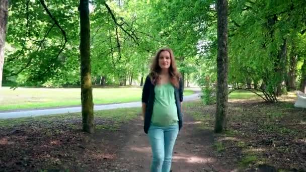 Pregnant woman expectant mother walking through park tree alley — Stock Video