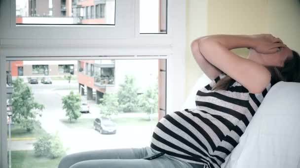 Utmattad gråtande gravid kvinna sitter på soffa nära fönster — Stockvideo